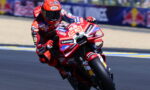 Motorcycle racer leaning into a turn on a red race bike covered in sponsor logos (Lenovo, Shell) on a race track Vieira Biker scene