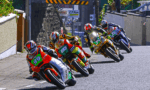 Group of motorcycle racers on a street circuit leaning into a corner in a tight pack.