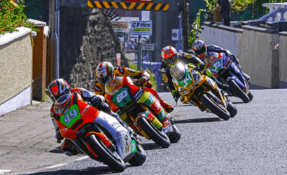 Group of motorcycle racers on a street circuit leaning into a corner in a tight pack.