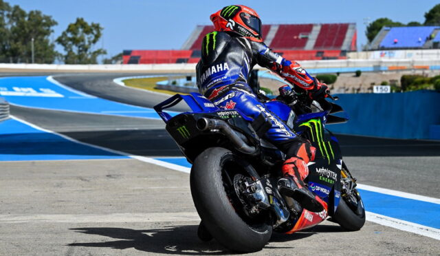 Moto racer on a blue Yamaha bike leaning into a turn on a race track; Monster Energy livery and red helmet visible.