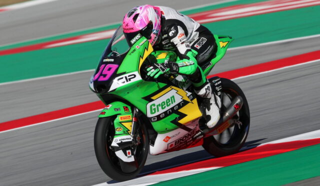 MotoGP rider in a pink helmet leans into a corner on a bright green race bike with 'Green energy' branding, number 19 visible on the front plate.