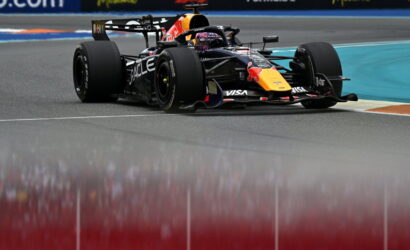 Red Bull Racing Formula 1 car taking a tight corner on a race track, sponsor logos visible on the car and barriers in the background
