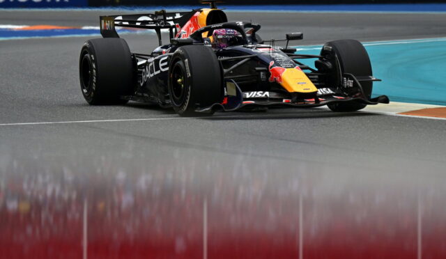 Red Bull Racing Formula 1 car taking a tight corner on a race track, sponsor logos visible on the car and barriers in the background