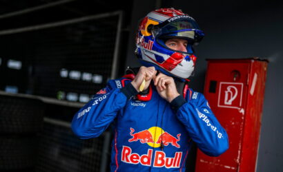 Formula 1 driver in a Red Bull blue racing suit tightens his helmet in a garage.