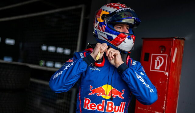 Formula 1 driver in a Red Bull blue racing suit tightens his helmet in a garage.