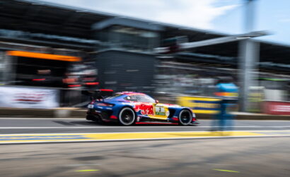 Blue-and-red race car with sponsor decals speeds along the pit lane, background blurred by motion.