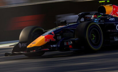 Red Bull Racing Formula 1 car zooming on track, orange nose with Red Bull logo and sponsor decals visible.