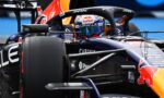 Formula 1 race car close-up: cockpit with Red Bull branding, helmeted driver visible behind the steering wheel, sponsor logos around the fuselage.