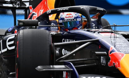 Formula 1 race car close-up: cockpit with Red Bull branding, helmeted driver visible behind the steering wheel, sponsor logos around the fuselage.