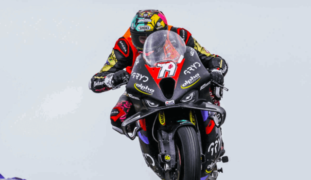 Motorcycle racer in colorful gear performing a mid-air jump on a sport bike during a race event.