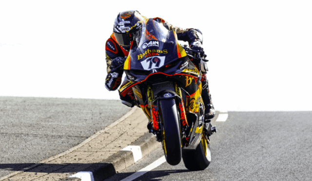 Sport motorcycle racer in full leathers leans into a left-hand bend, front wheel lifted off the road during a high-speed turn on a track-like roadway.