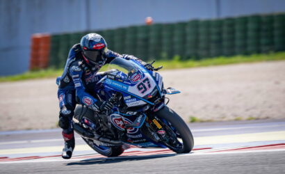 Motorcycle racer in blue gear leaning into a turn on a racing track, bike number 97 with sponsor logos visible