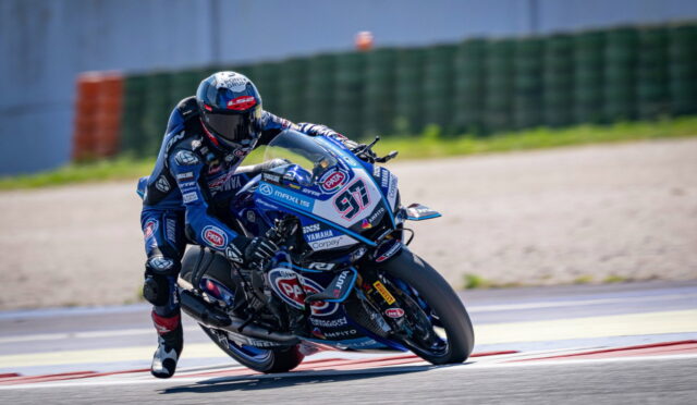 Motorcycle racer in blue gear leaning into a turn on a racing track, bike number 97 with sponsor logos visible