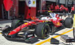 Red Ferrari Formula 1 car in the pit lane with crew members in red shirts and pit equipment nearby, ready for service.