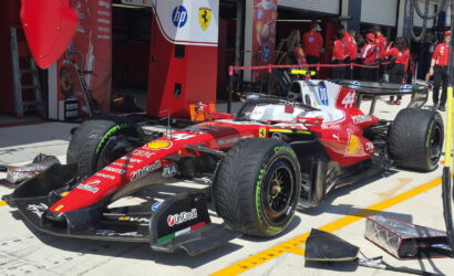 Red Ferrari Formula 1 car in the pit lane with crew members in red shirts and pit equipment nearby, ready for service.