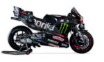 Racing sport motorcycle with sponsor logos on a stand, black and blue livery featuring Monster Energy and Aprilia branding.