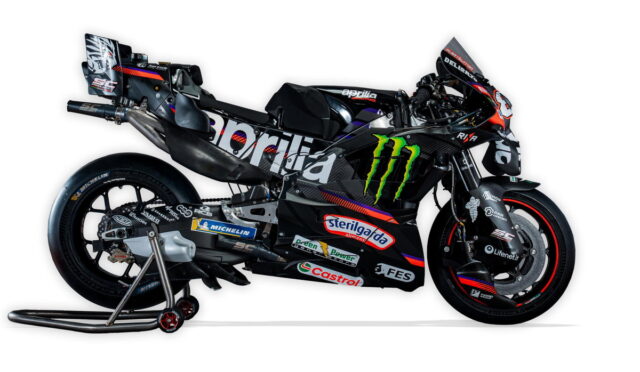 Racing sport motorcycle with sponsor logos on a stand, black and blue livery featuring Monster Energy and Aprilia branding.
