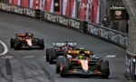 Three Formula 1 cars race on a street circuit with barriers advertising TAG Heuer in the background.