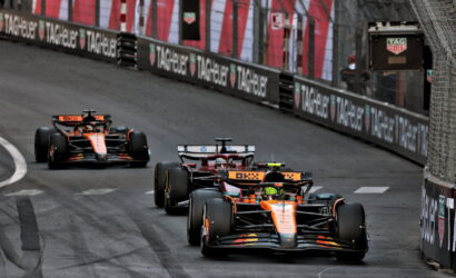 Three Formula 1 cars race on a street circuit with barriers advertising TAG Heuer in the background.