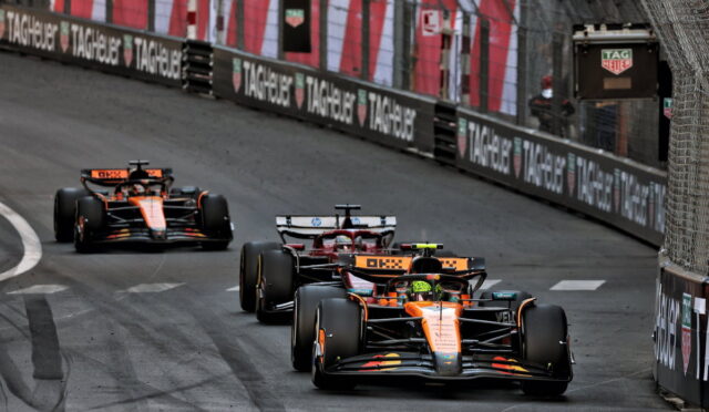 Three Formula 1 cars race on a street circuit with barriers advertising TAG Heuer in the background.