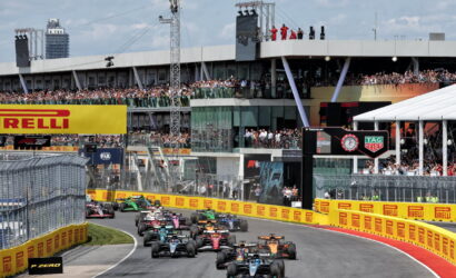 Formula 1 cars race down a street circuit with grandstands full of spectators and prominent sponsor banners (Pirelli).