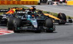 Mercedes-AMG Petronas F1 car leads a group around a track corner, with other teams close behind.
