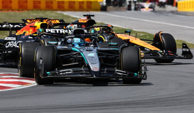 Mercedes-AMG Petronas F1 car leads a group around a track corner, with other teams close behind.