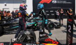Two Formula 1 drivers share a fist bump beside their race cars on the pit lane, with photographers and a FIA banner in the background.