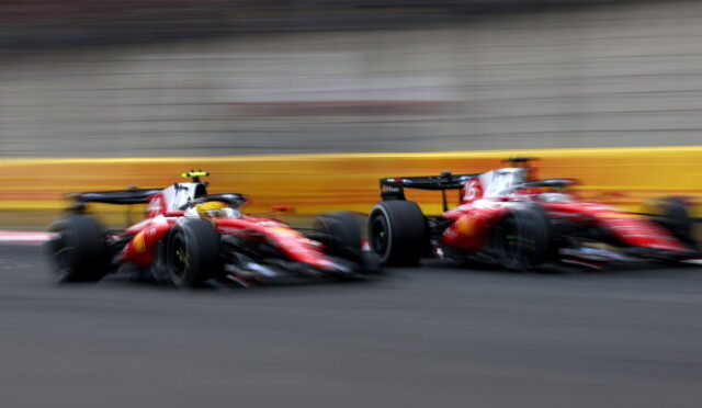 Two red Formula 1 cars sprinting along a race track, motion blur showing high speed and a yellow barriers in the background.