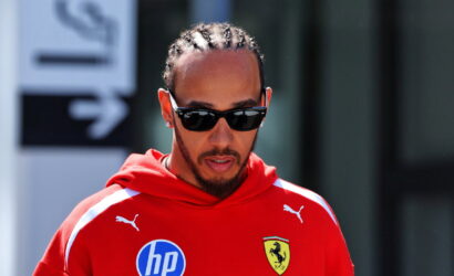 Man with cornrow braids wearing black sunglasses and a red Ferrari hoodie with an HP logo on the chest.