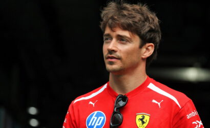 Portrait of a man in a red Ferrari polo shirt with sponsor logos, sunglasses clipped to the chest, looking off to the side.