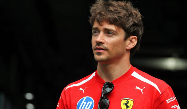 Portrait of a man in a red Ferrari polo shirt with sponsor logos, sunglasses clipped to the chest, looking off to the side.