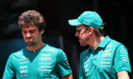 Two men in teal team uniforms stand outdoors; one on the left squints with a frown while the other on the right wears a teal cap and speaks to him.