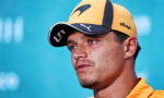 Close-up of a man wearing a yellow cap and orange shirt, looking off to the side against a blue background.
