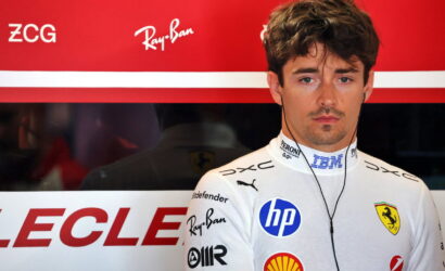 Portrait of a Ferrari Formula 1 driver in a white racing suit with sponsor logos, wearing earphones against a red backdrop.