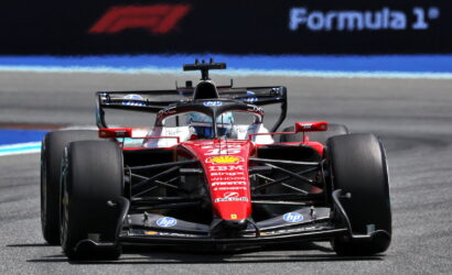 Front view of a red Formula 1 car racing toward the camera on the track, sponsorship logos visible in red livery.