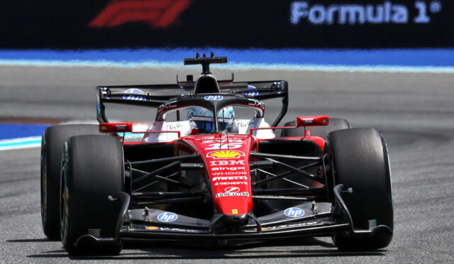 Front view of a red Formula 1 car racing toward the camera on the track, sponsorship logos visible in red livery.