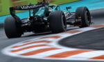 Green Formula 1 car speeds through a corner, rear view with Valvoline branding and blurred curbstones in the foreground