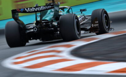 Green Formula 1 car speeds through a corner, rear view with Valvoline branding and blurred curbstones in the foreground