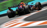 Formula 1 car speeding on a racetrack with motion blur, Oracle branding on the rear wing and bright orange-green surroundings behind the vehicle.