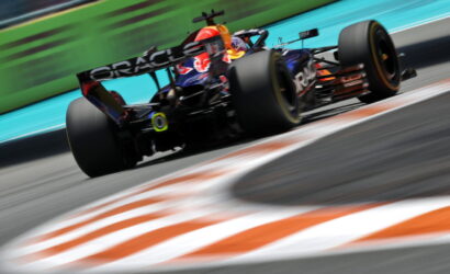 Formula 1 car speeding on a racetrack with motion blur, Oracle branding on the rear wing and bright orange-green surroundings behind the vehicle.