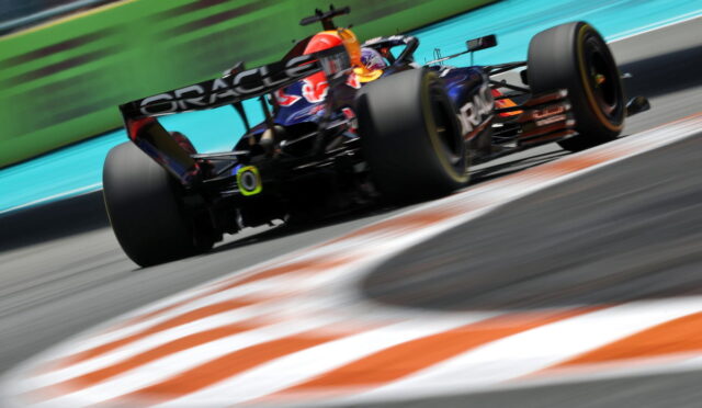 Formula 1 car speeding on a racetrack with motion blur, Oracle branding on the rear wing and bright orange-green surroundings behind the vehicle.
