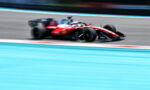 Red Formula 1 car racing at high speed on a track, with motion blur emphasizing speed and a turquoise runoff area nearby.