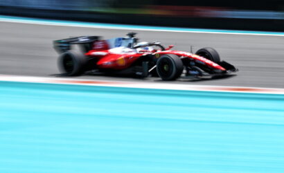 Red Formula 1 car racing at high speed on a track, with motion blur emphasizing speed and a turquoise runoff area nearby.