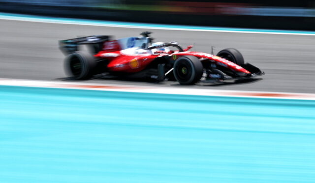 Red Formula 1 car racing at high speed on a track, with motion blur emphasizing speed and a turquoise runoff area nearby.