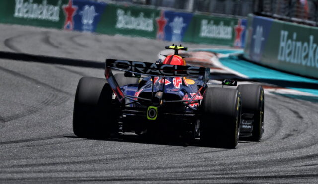 Red Bull Formula 1 car seen from behind on a race track, rear wing with ORACLE text and Heineken banners along the barrier nearby
