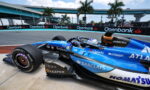 Blue Formula 1 car on a race track with Openbank banners along the barriers in the background.