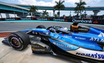 Blue Formula 1 car on a race track with Openbank banners along the barriers in the background.