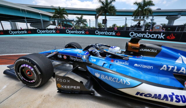 Blue Formula 1 car on a race track with Openbank banners along the barriers in the background.