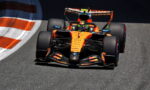 Orange Formula 1 race car speeding along a track, front view with large rear wing and slick tires on asphalt edge of a curve
